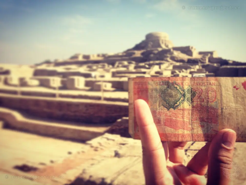 The 20 rupee note held up against the ruins of Mohenjodaro